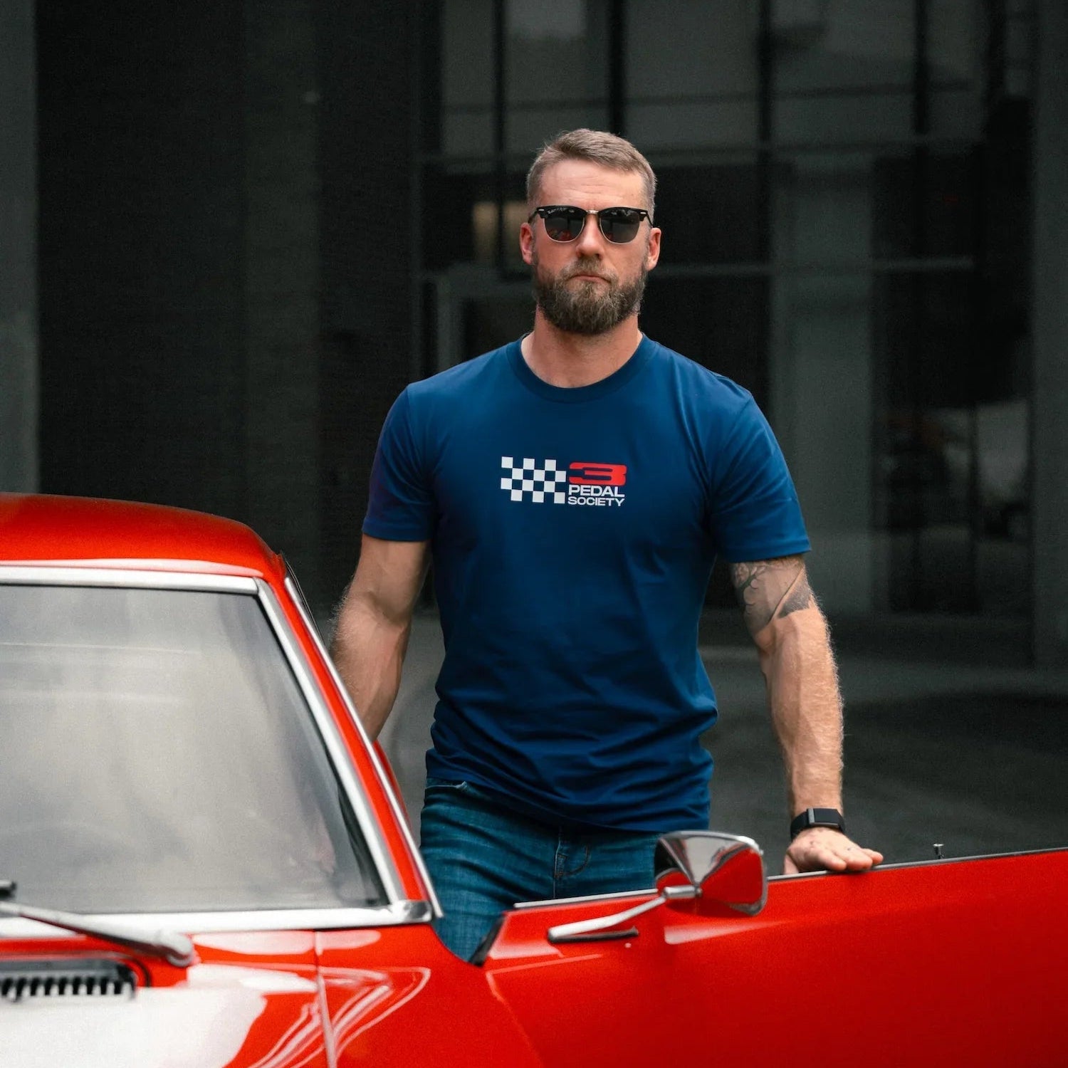 Man in a blue t-shirt standing next to a red car with a dark background