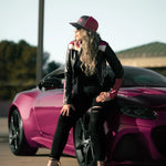 Woman posing next to a pink car on a road