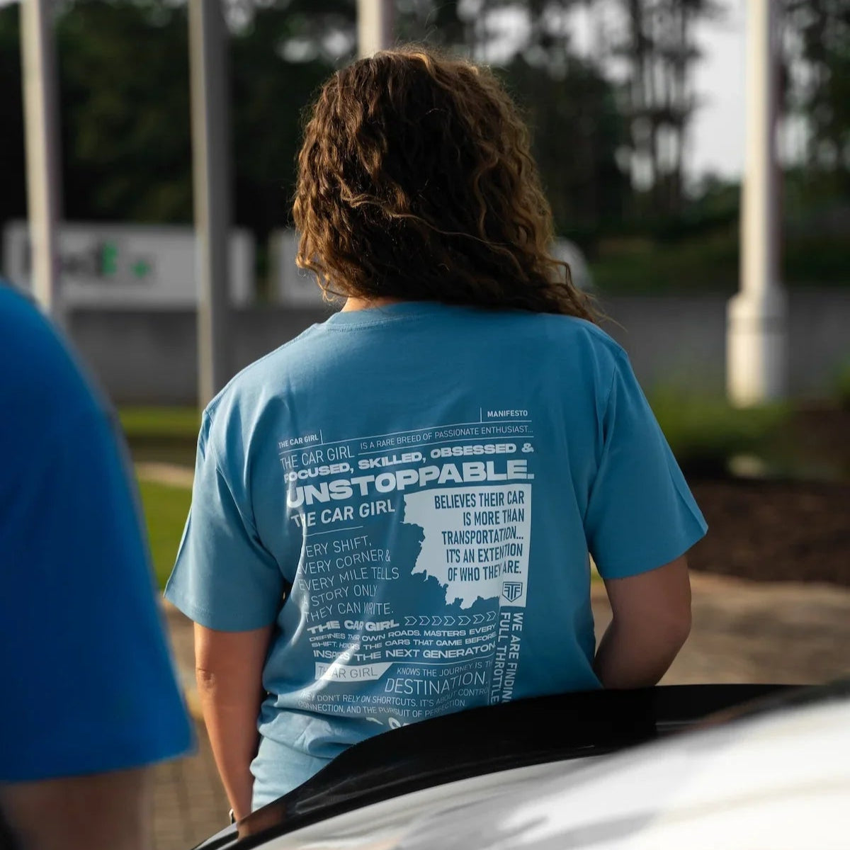 Person wearing a blue t-shirt with text standing next to a car