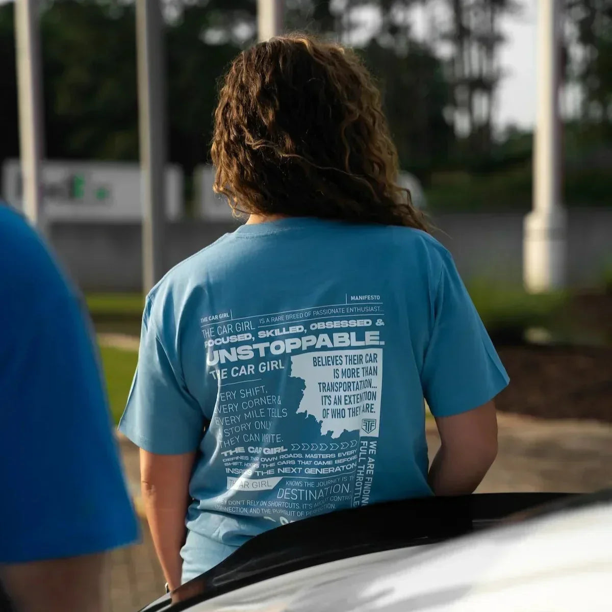 Person wearing a blue t-shirt with text standing next to a car