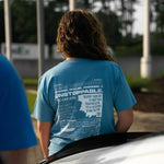 Person wearing a blue t-shirt with text standing next to a car