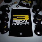 Collection of '3 Pedal Society' merchandise including hats and a towel on a dark background.