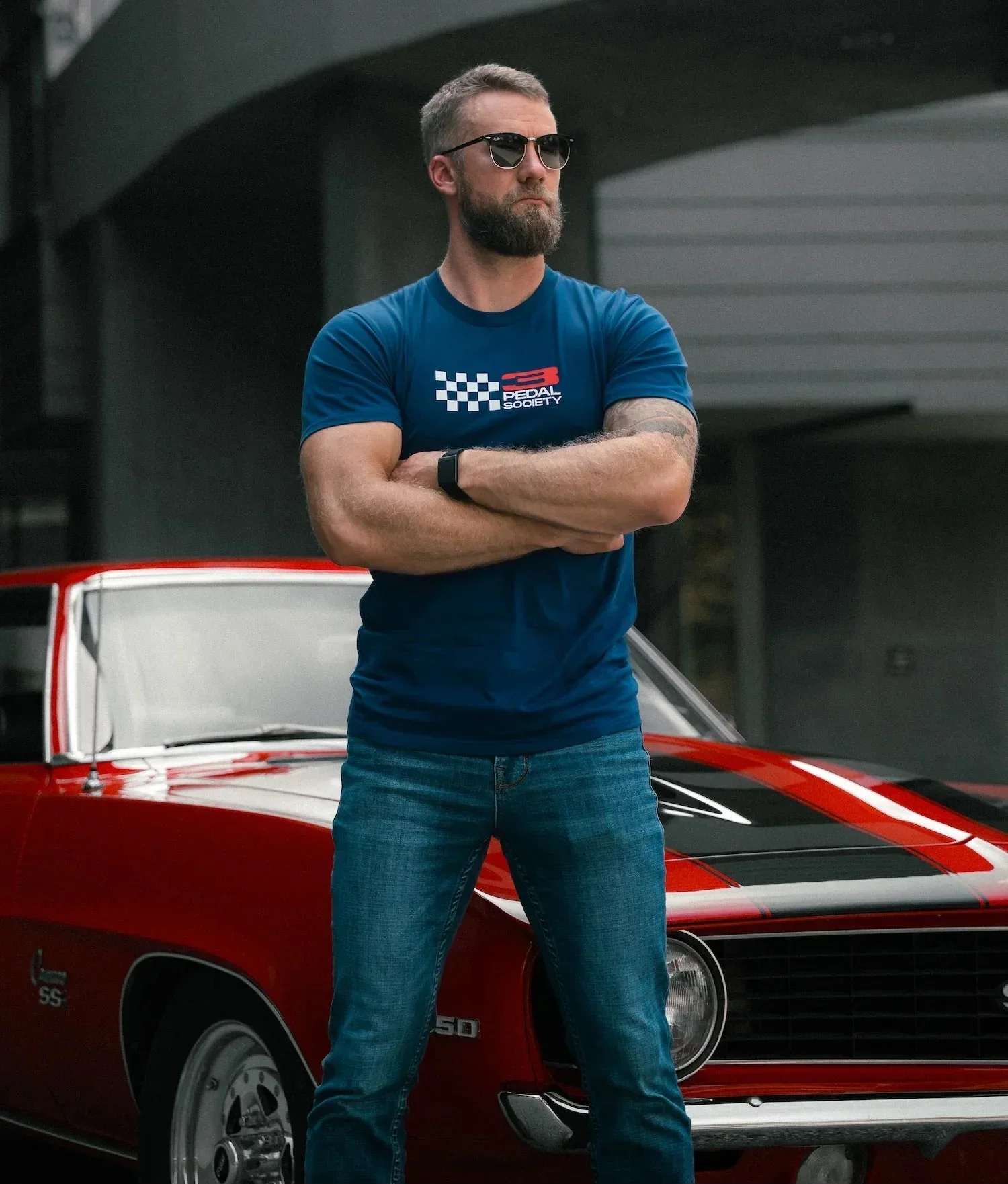 Man wearing a blue t-shirt with a logo standing in front of a red car.