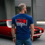 Man wearing a blue t-shirt with '3 Pedal Society' logo in front of a red car.