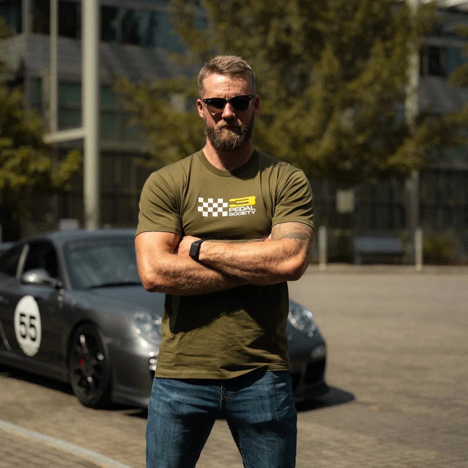 Man standing with arms crossed in front of a car, wearing a green t-shirt and sunglasses.