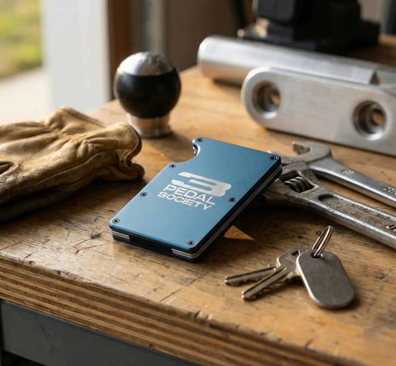 Blue cardholder with '3 Pedal Society' branding on a wooden surface with tools and keys.