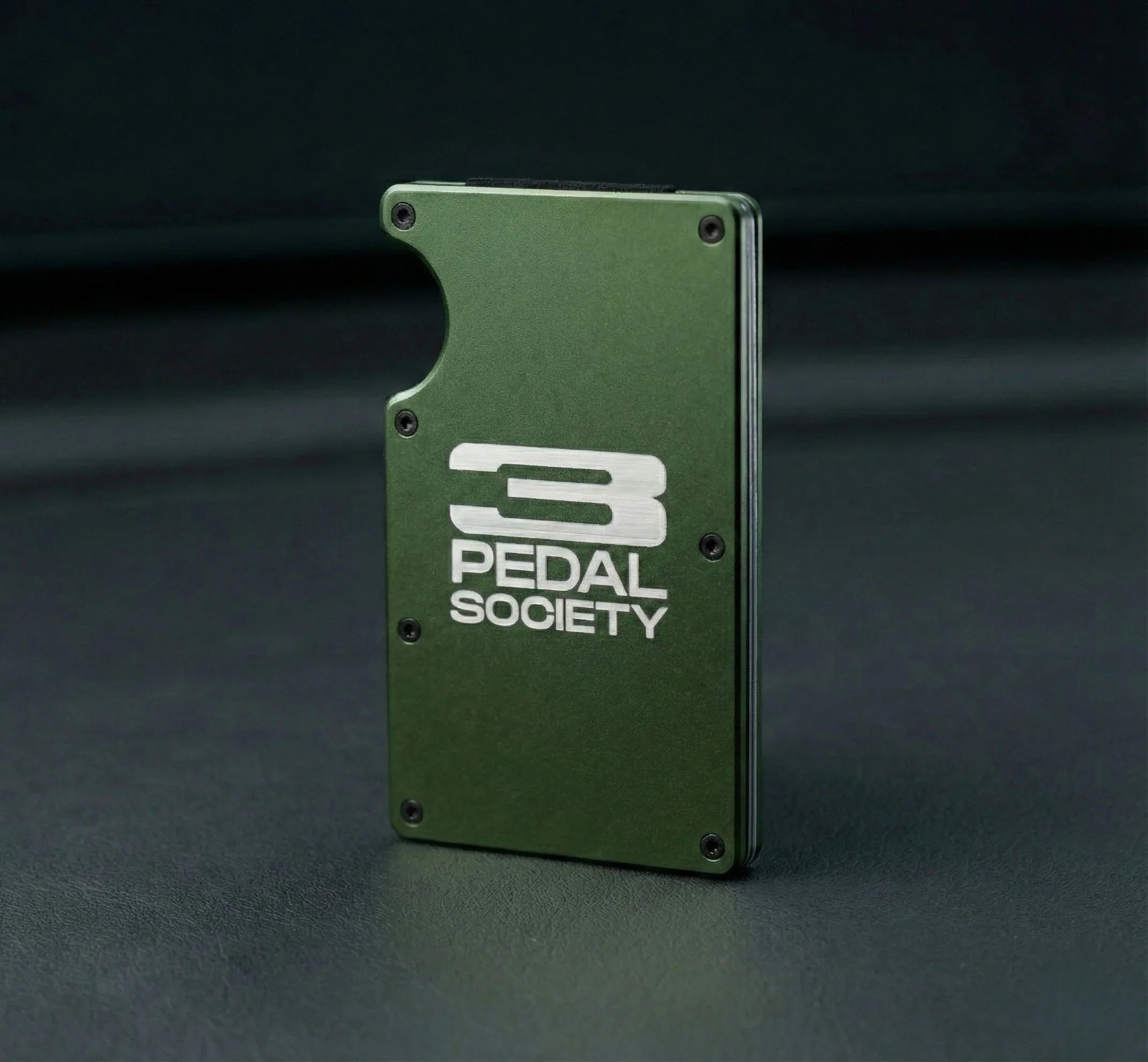 Green metal wallet with '3 Pedal Society' logo on a dark background