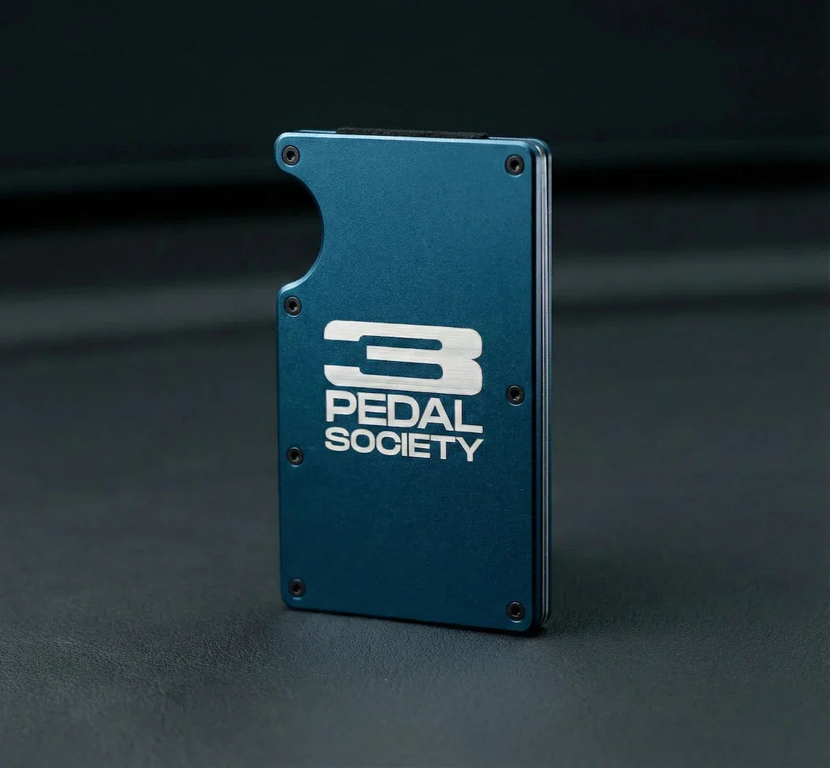 Blue metal bracket with '3 Pedal Society' logo on a dark background