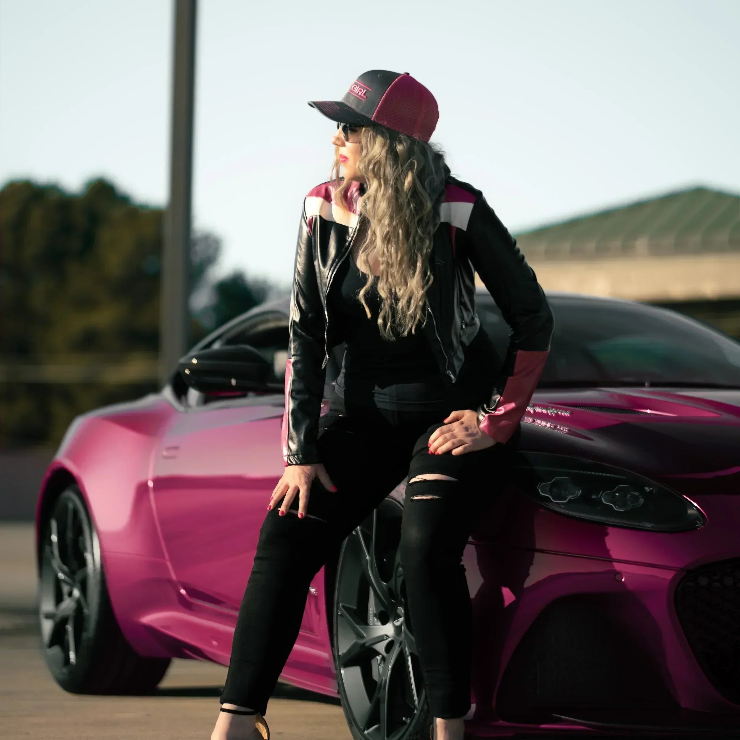 Woman posing next to a pink car on a road