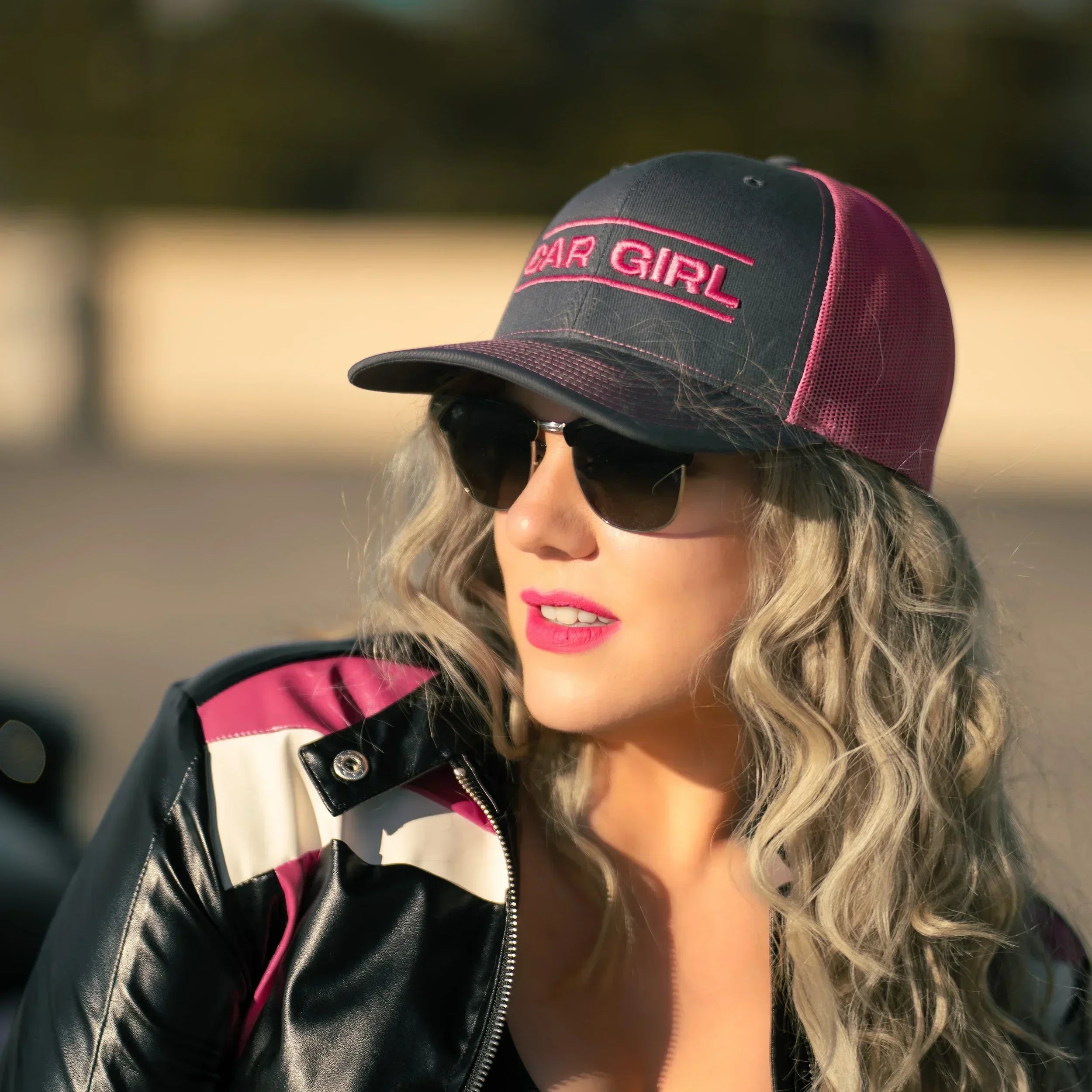 Woman wearing a cap with 'Car Girl' text and sunglasses outdoors