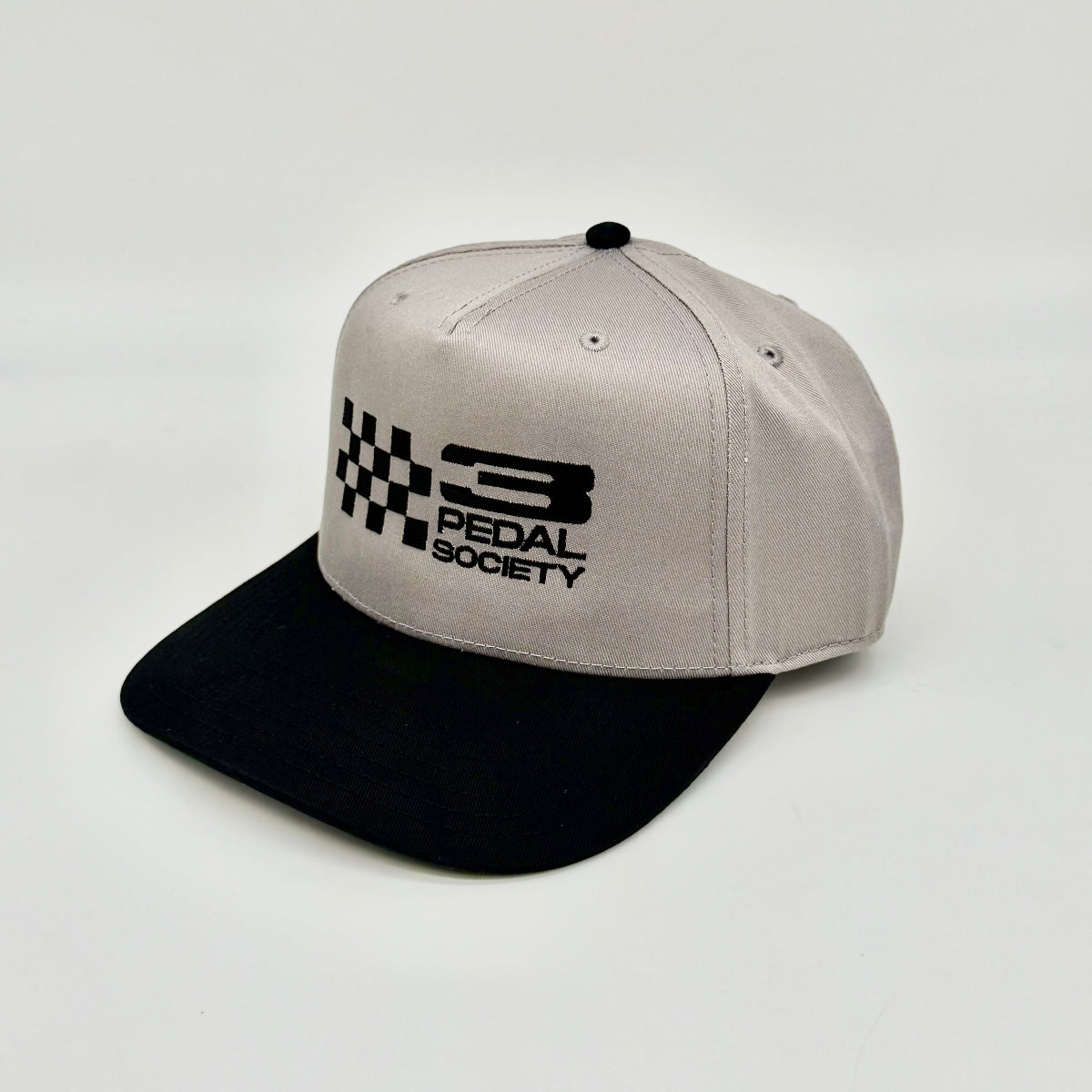 A structured snapback cap with a light gray crown and a black flat brim, featuring a black embroidered logo that reads '3 PEDAL SOCIETY' alongside a checkered flag motif on the front.