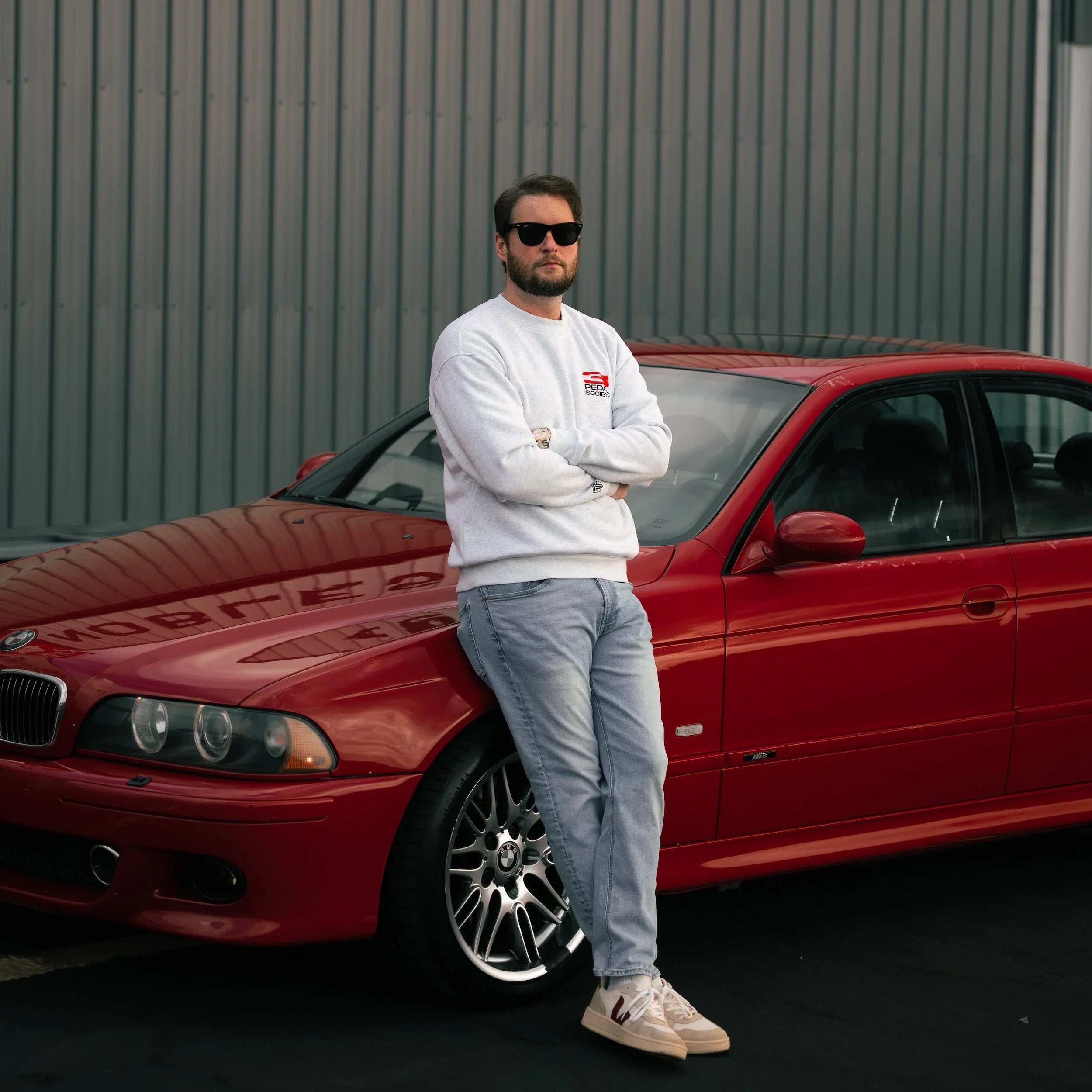 Man standing next to a red car in front of a gray building