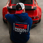 Person wearing a hoodie with '3 Pedal Society' logo in front of a red car.