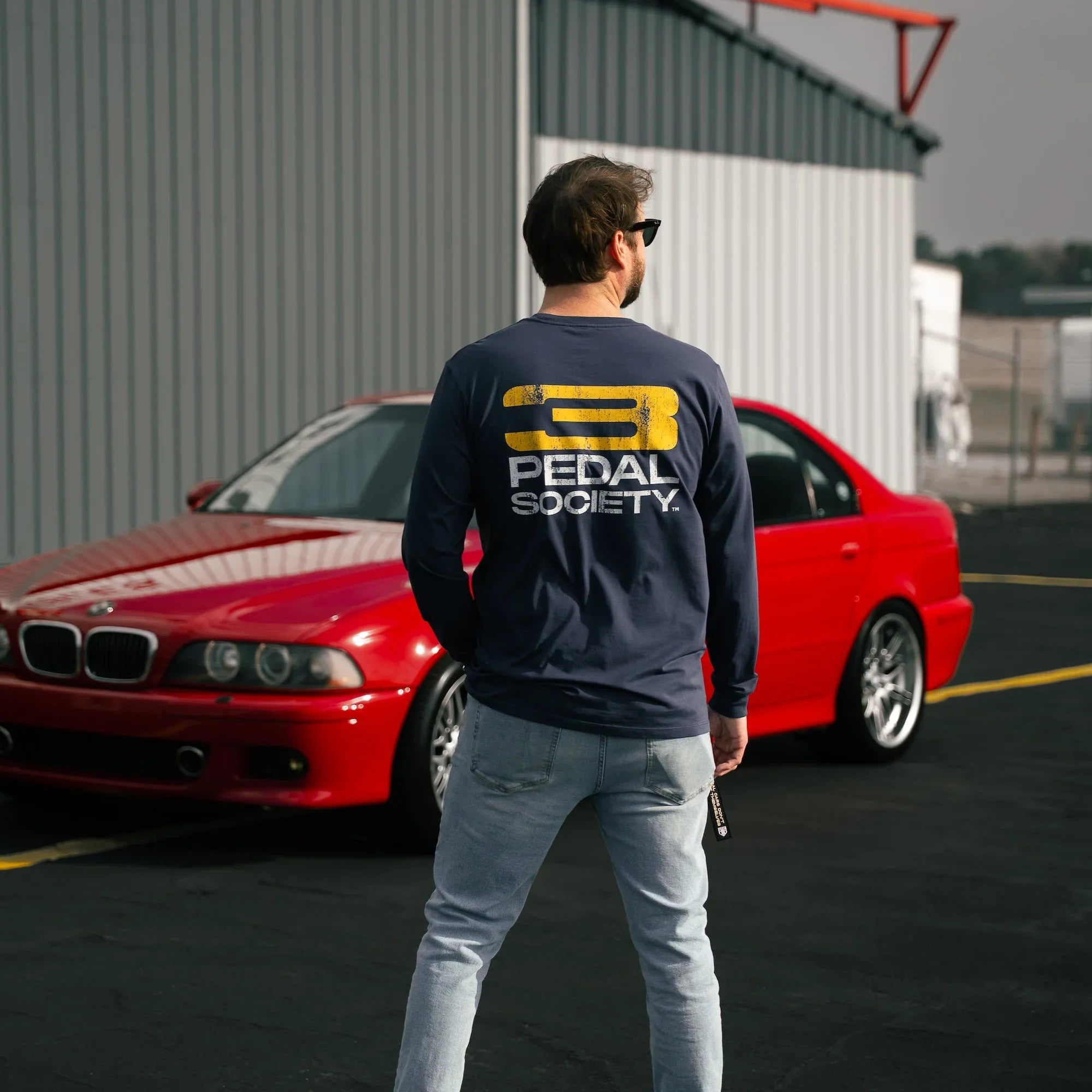 Man wearing a '3 Pedal Society' shirt standing in front of a red car.