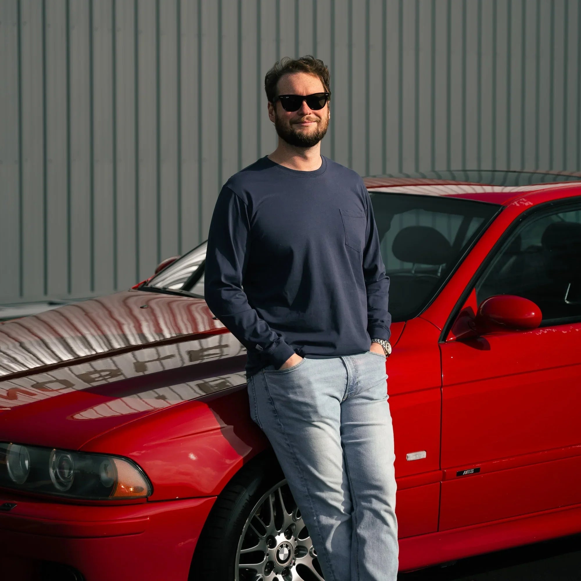 Man standing next to a red car with a gray building in the background