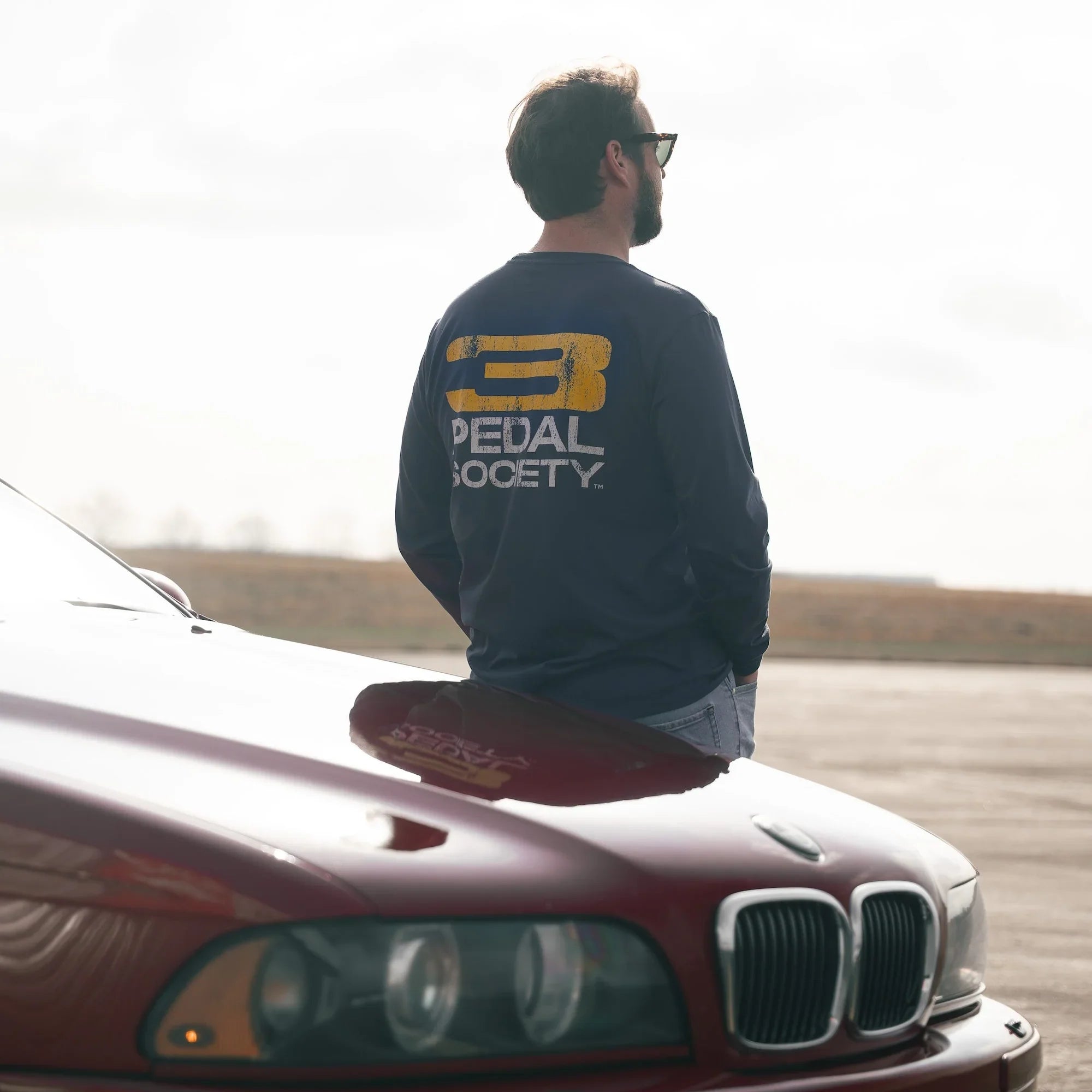 Man sitting on a red car with 'Pedal Society' logo on a white background