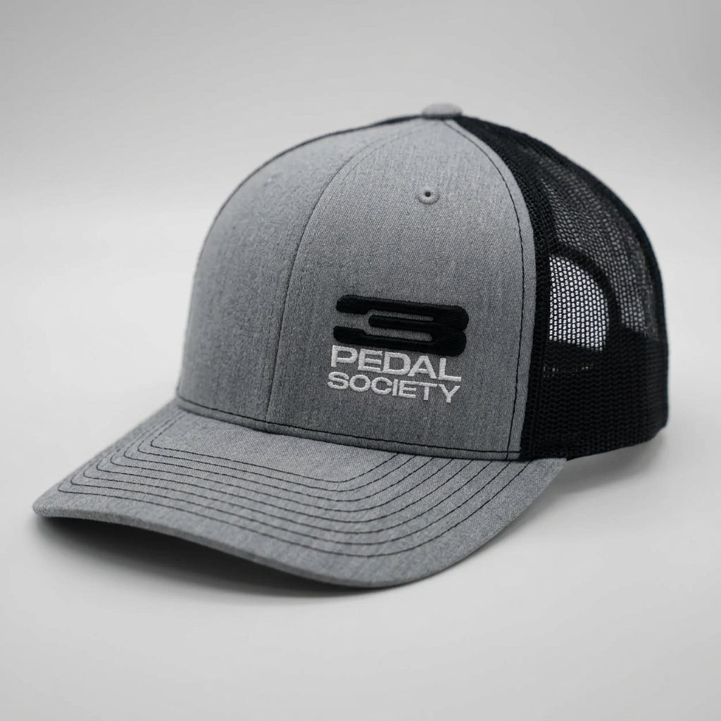 A heather gray and black trucker hat with a structured gray front panel, black mesh back, and a black and white embroidered 'PEDAL SOCIETY' logo on the front.