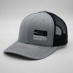 A heather gray and black trucker hat with a structured gray front panel, black mesh back, and a black and white embroidered 'PEDAL SOCIETY' logo on the front.