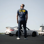 Person wearing a branded t-shirt standing on a track with a car in the background