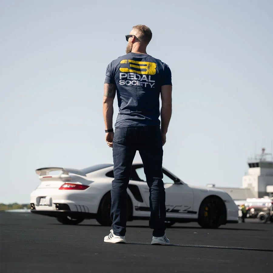 Person wearing a branded t-shirt standing on a track with a car in the background