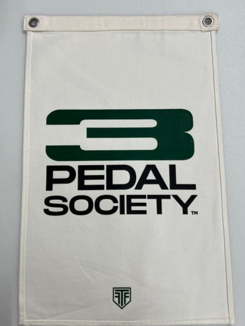 An off-white canvas flag featuring the dark green and black 'Pedal Society' logo, with metal grommets on the left side, shown against a neutral gray background.
