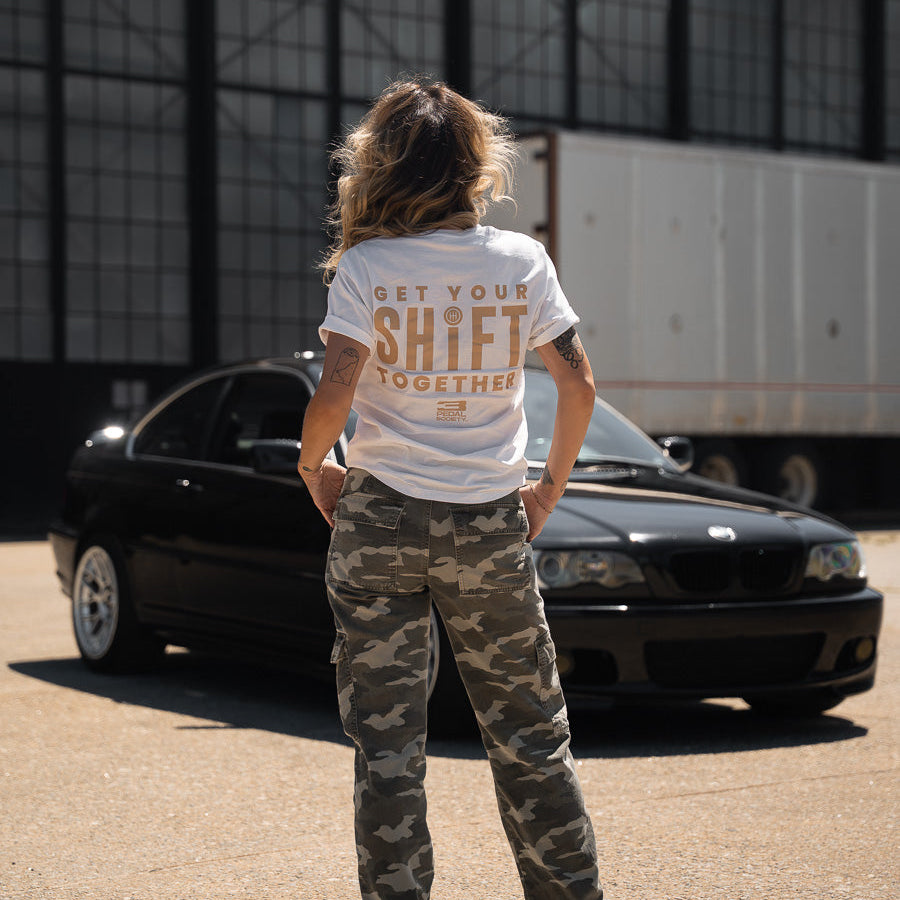 Person wearing a white t-shirt with text standing in front of a black car.