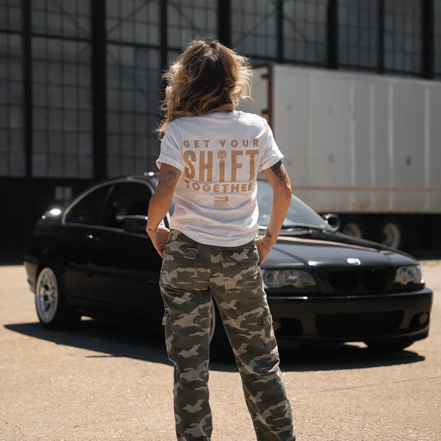 Person wearing a white t-shirt with text standing in front of a black car.