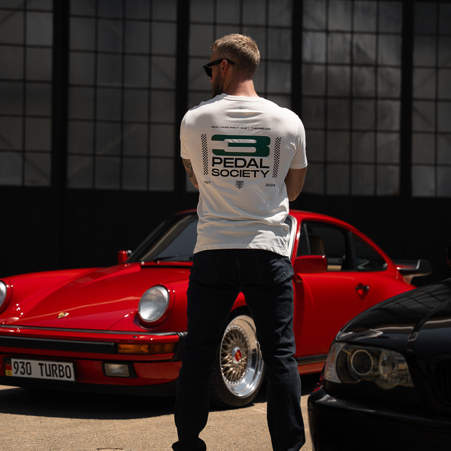 Man wearing a 'Pedal Society' t-shirt standing next to a red Porsche 930 Turbo.