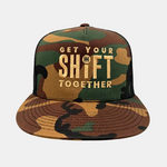 A camouflage trucker hat with a flat brim and black mesh back, featuring the text 'GET YOUR SHIFT TOGETHER' in gold lettering on the front panel.