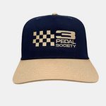 A structured baseball cap with a dark navy blue crown and a beige brim, featuring a gold embroidered checkered flag and the '3 PEDAL SOCIETY' logo on the front.